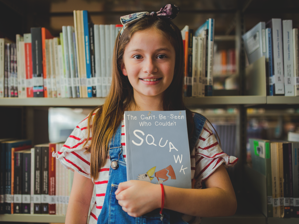 happy-little-girl-holding-a-can't-be-seen-who-couldn't-squawk-book-mockup-at-the-library-a19273